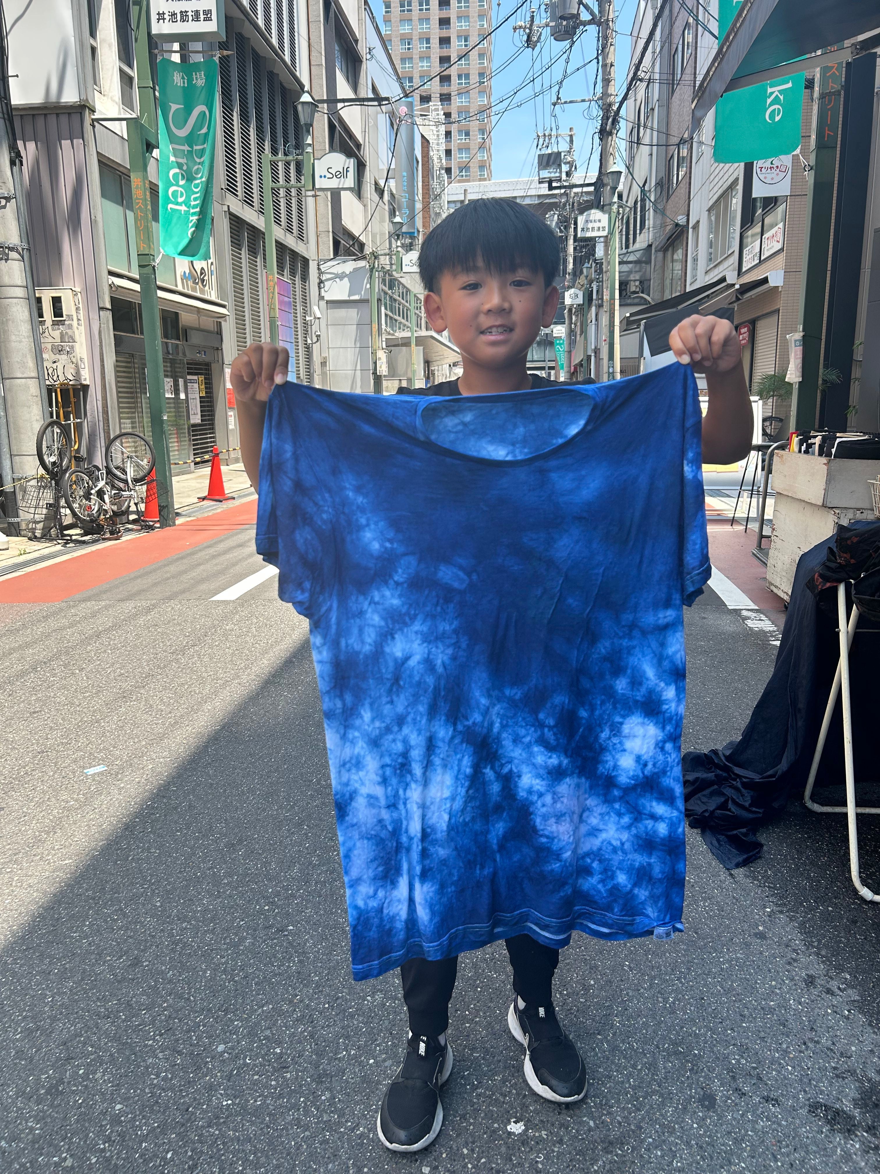 Child holding a blue tie-dye shirt on a city street